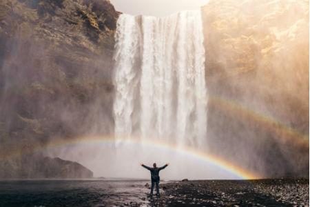 Guy standing under a waterfall with a rainbow